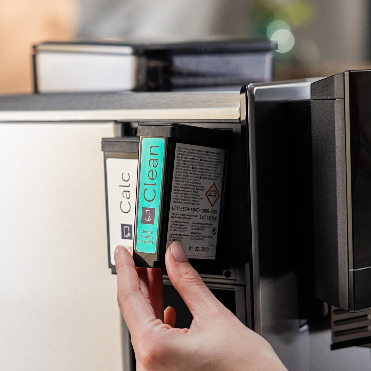 Siemens Čisticí patrona pro EQ900 plus (TZ800Z1) — ruka vkládá černou patronu s modrozeleným štítkem "Clean" do přihrádky