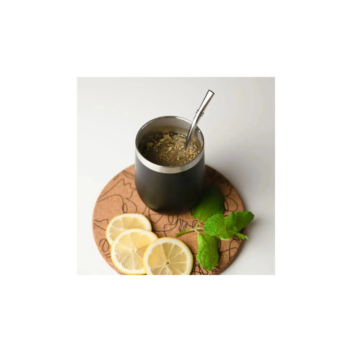 Aquafloow Black Yerba Maté thermocup 355 ml with stainless straw, filled with yerba, on a cork coaster with lemon slices