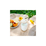 Aquafloow 500 ml glass in a white silicone sleeve with a wooden lid and a white straw on a picnic blanket next to a plate with