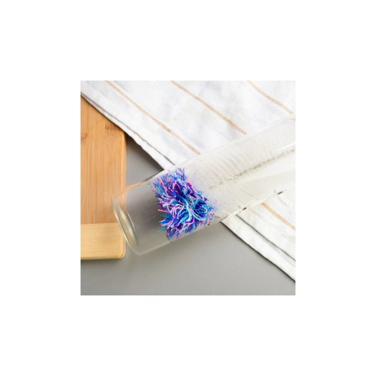 Aquafloow Bottle cleaning brush for carbonators – transparent bottle lying on fabric with blue‑purple brush head