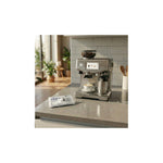 Aquafloow descaling tablets for coffee machines, kettles and irons (4 pcs) – tablet pack placed next to a stainless coffee machine on a counter
