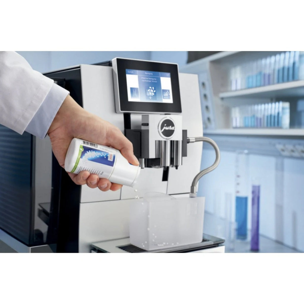 JURA Čisticí mini tablety pro mléčný systém s dávkovačem 90g (24158) – ruka drží lahvičku nad mléčným vývodem automatu a