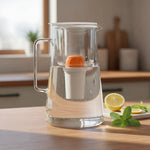 Glass filter pitcher with handle, internal white filter cartridge with orange lid filled with water on a kitchen counter